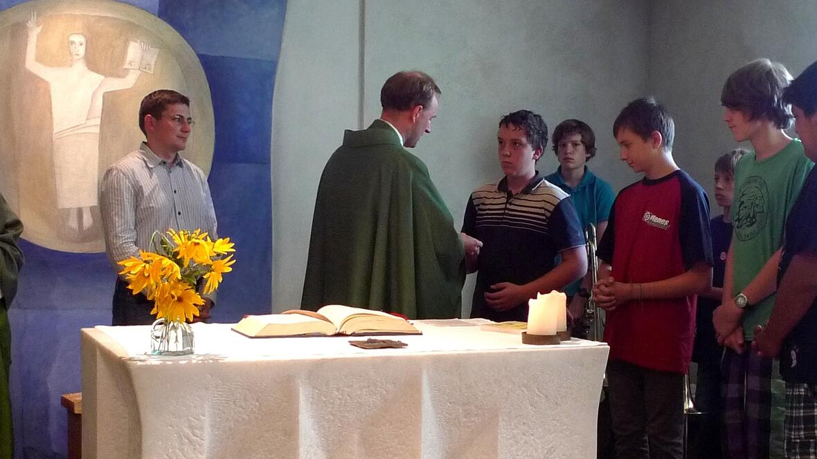 Pfarrer Bernhard Waltner überreicht an einen Teilnehmer des Sommerkurses das Kreuz des Offenen Seminars.