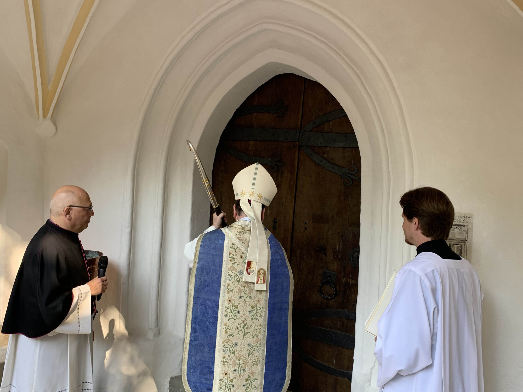 Bischof Meier klopft mit seinem Bischofsstab an die Kirchentüre, um diese zu öffnen.