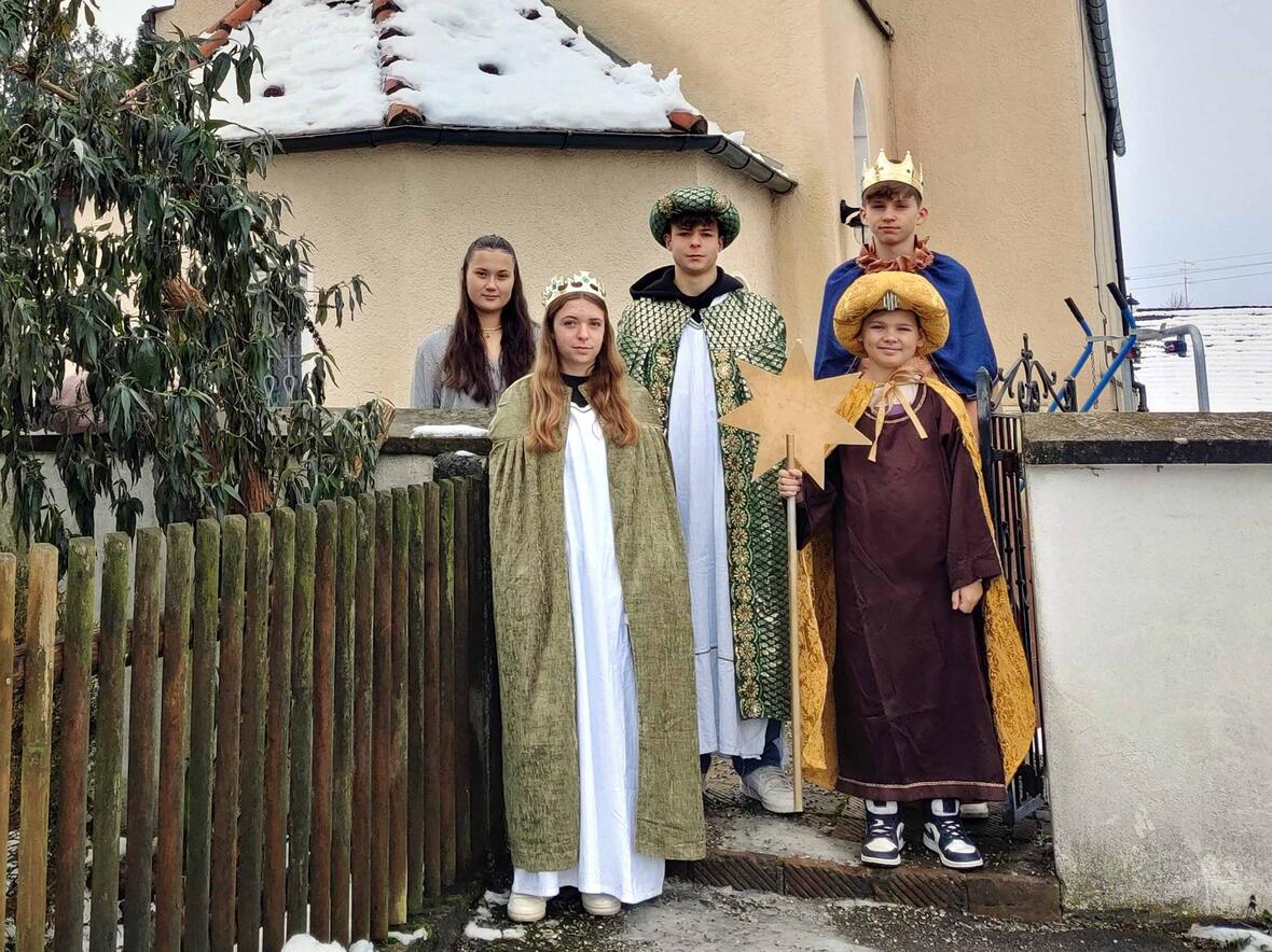 Vor der Pfarrkirche St. Ursula und Gefährtinnen und dem historischen Pfarrhof in Rommelsried stehen (von rechts nach links) die Sternsingerinnen und Sternsinger Simon (14), Nils mit dem Stern (13), Valentin (15) Magdalena (15) und Begleiterin Clarissa (18). (Foto: PG Dietkirch)